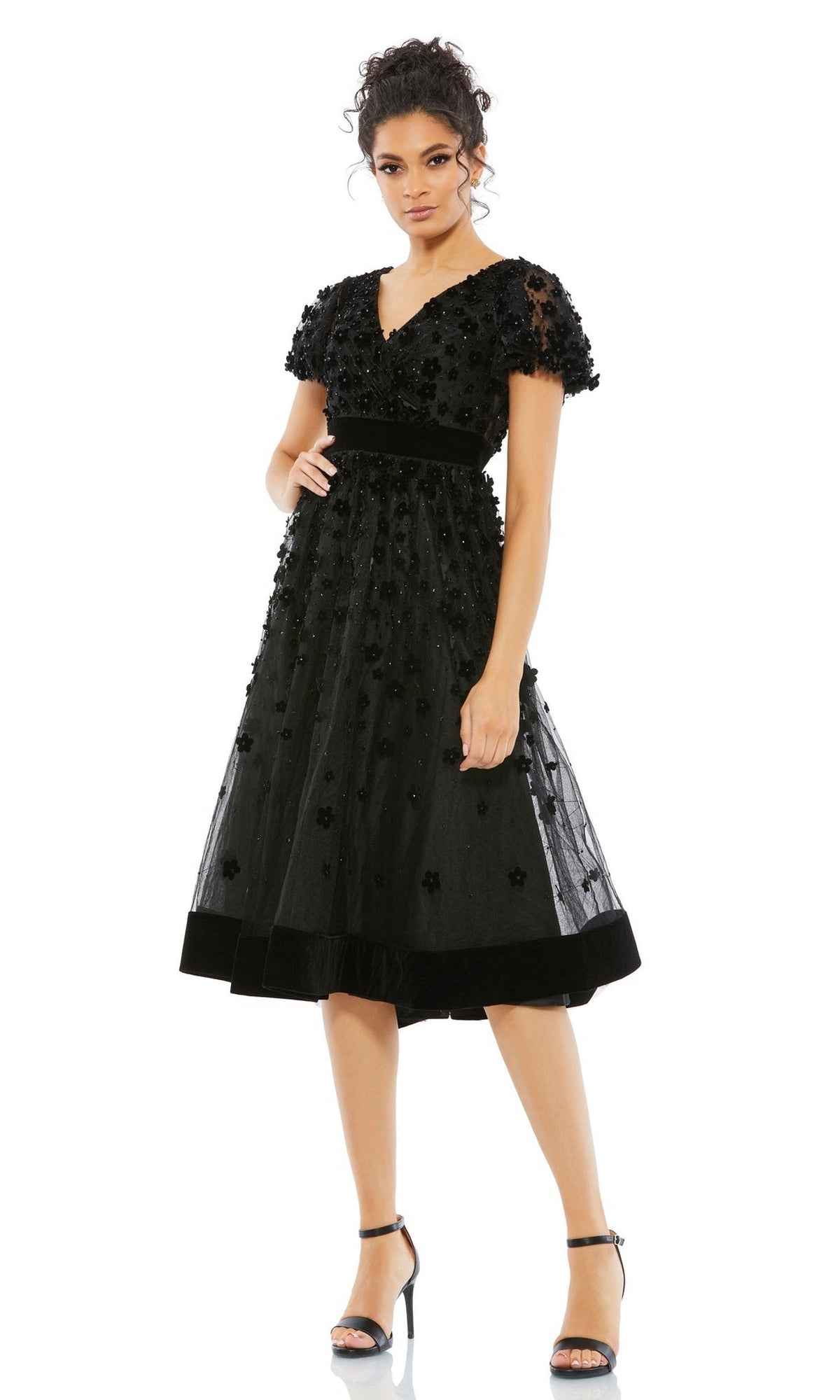 A woman wearing the Mac Duggal 67854 Floral Midi Wedding Guest Dress with black floral embellishments, short sleeves, and vintage knee-length style stands in heels against a plain white background.